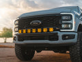 Leveled gray Ford Super Duty at sunset featuring the Lewis Built Performance APEX bumper light mount with seven bright amber auxiliary lights.