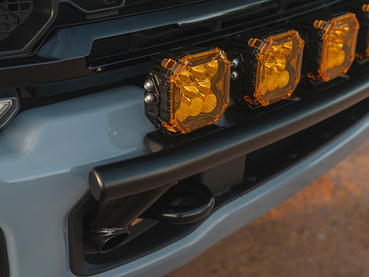 Close-up of seven amber LED off-road lights mounted on a black Lewis Built Performance APEX light mount on the front bumper of a leveled gray Ford Super Duty.