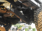Close-up of heavy-duty Lewis Built Performance Ford Super Duty radius arms connected with Grade 8 bolts and rod ends, with aftermarket shock absorbers visible, set against reddish-brown dirt.