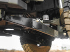 Close-up of heavy-duty Lewis Built Performance Ford Super Duty radius arms connected with Grade 8 bolts and rod ends, with aftermarket shock absorbers visible, set against reddish-brown dirt.