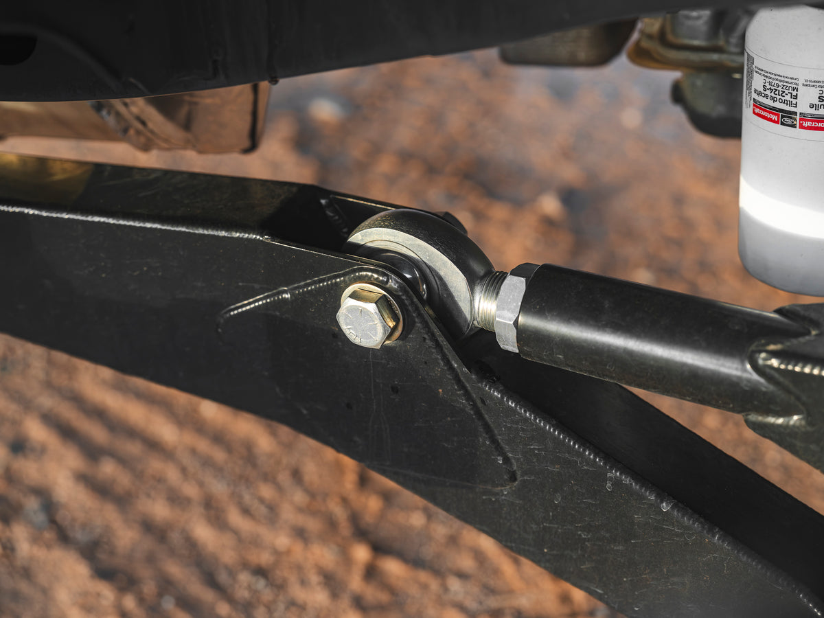 Close-up of heavy-duty Lewis Built Performance Ford Super Duty radius arms connected with Grade 8 bolts and rod ends, set against reddish-brown dirt.