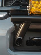 Close-up of a black Lewis Built Performance APEX bumper light mount installed on a leveled gray Ford Super Duty, with part of a bright amber off-road light visible above.